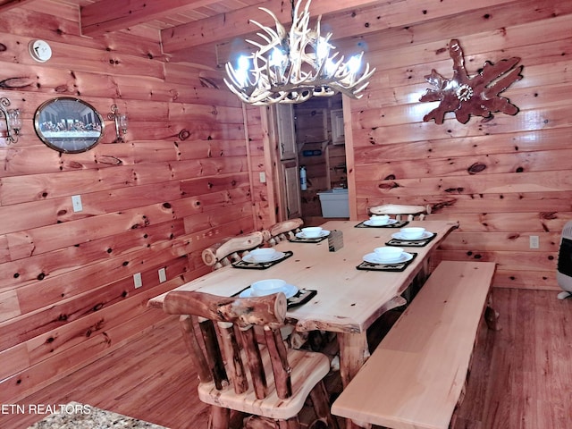 dining space with a chandelier, wood finished floors, beam ceiling, and wooden walls