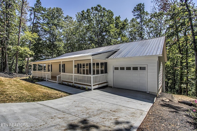 ranch-style house with a garage, covered porch, metal roof, and concrete driveway