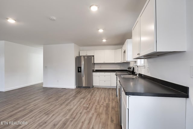 kitchen featuring a sink, white cabinetry, light wood-style floors, stainless steel fridge with ice dispenser, and dark countertops