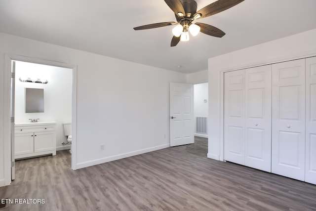 unfurnished bedroom featuring ensuite bathroom, wood finished floors, visible vents, baseboards, and a closet