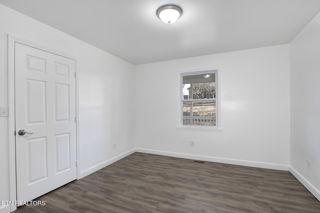 spare room with dark wood-style floors, visible vents, and baseboards