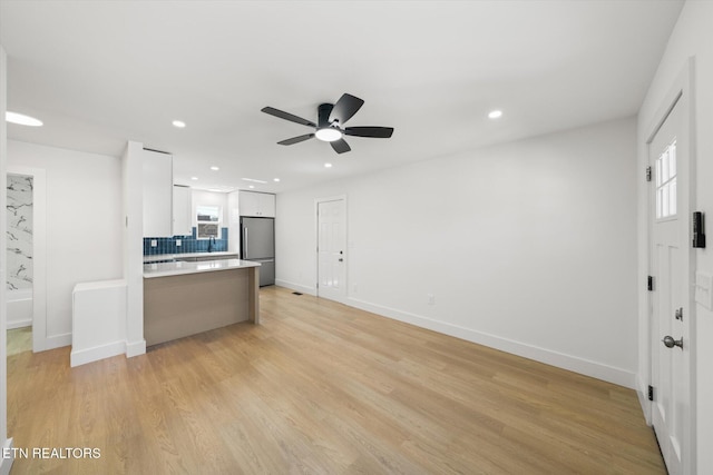 kitchen with light wood finished floors, stainless steel fridge, white cabinets, decorative backsplash, and a peninsula