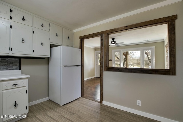 kitchen with baseboards, ceiling fan, light wood-type flooring, freestanding refrigerator, and white cabinets