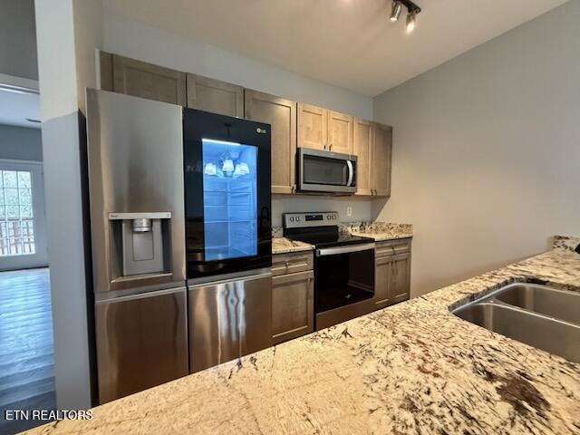 kitchen with light stone counters, track lighting, stainless steel appliances, and a sink