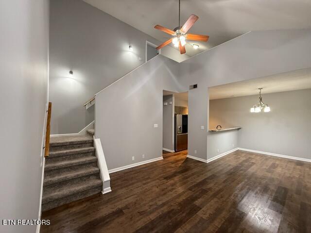 unfurnished living room featuring baseboards, wood finished floors, stairs, high vaulted ceiling, and ceiling fan with notable chandelier