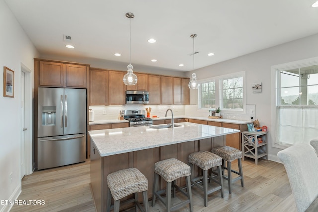 kitchen featuring light stone counters, stainless steel appliances, decorative backsplash, a sink, and light wood-type flooring