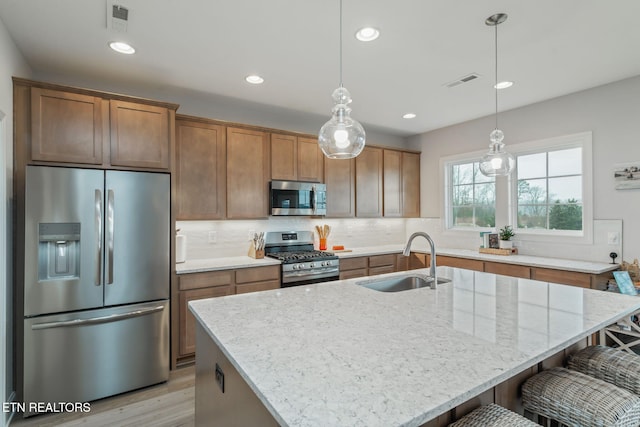 kitchen featuring light stone counters, visible vents, backsplash, appliances with stainless steel finishes, and a sink