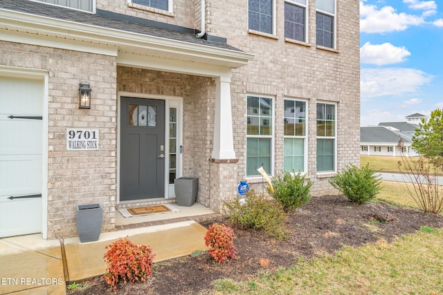 doorway to property with an attached garage, a shingled roof, and brick siding