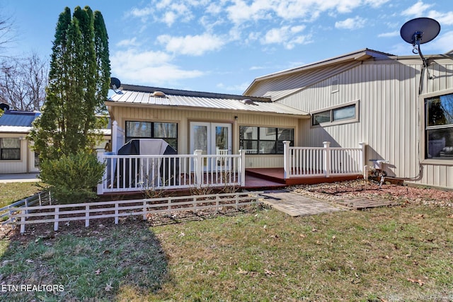 back of property with a wooden deck, a lawn, metal roof, and fence