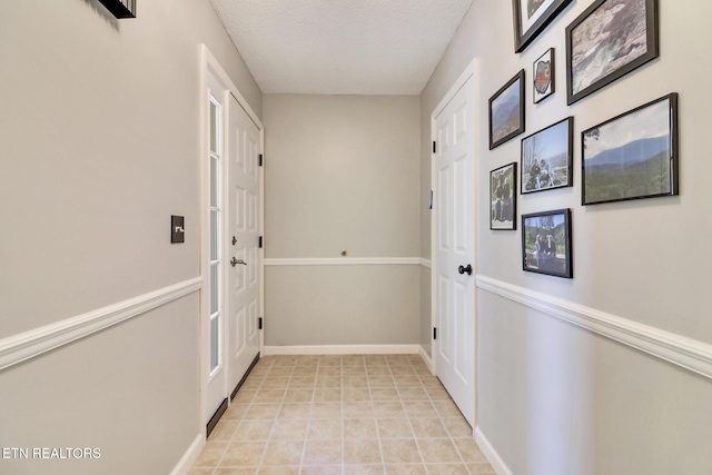 corridor with light tile patterned floors, a textured ceiling, and baseboards