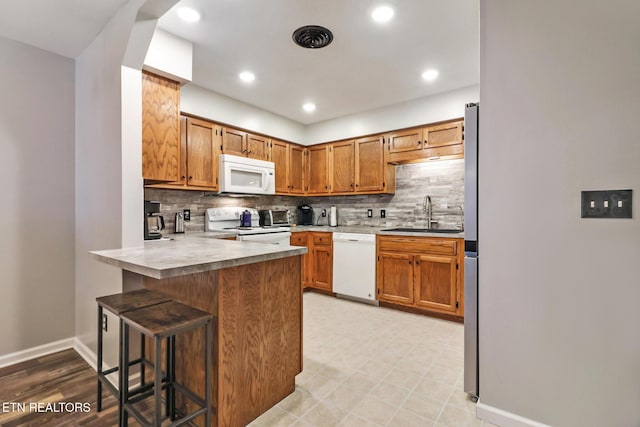 kitchen with a kitchen bar, a sink, backsplash, white appliances, and a peninsula