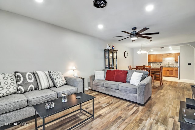 living area featuring light wood-style flooring, recessed lighting, ceiling fan with notable chandelier, and baseboards