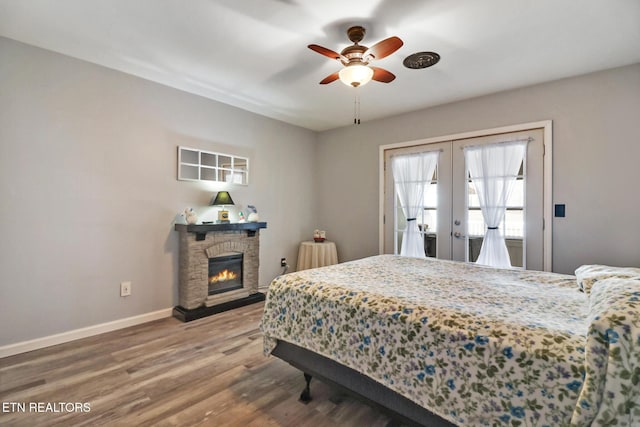 bedroom with wood finished floors, baseboards, a fireplace, ceiling fan, and french doors