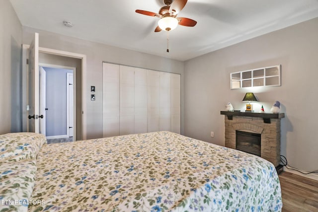 bedroom featuring a stone fireplace, wood finished floors, a closet, and a ceiling fan