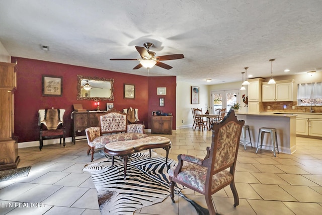 living area featuring light tile patterned floors, ceiling fan, a textured ceiling, and baseboards