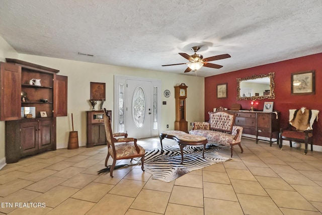 living area with a ceiling fan, light tile patterned flooring, and a textured ceiling