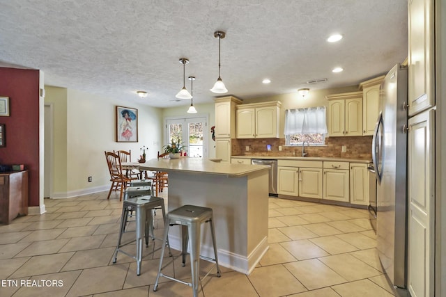 kitchen featuring cream cabinets, a breakfast bar area, light tile patterned flooring, stainless steel appliances, and decorative backsplash