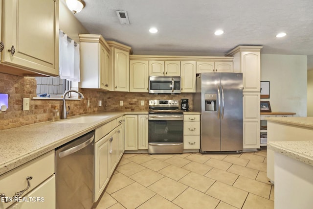 kitchen with stainless steel appliances, cream cabinetry, a sink, and decorative backsplash