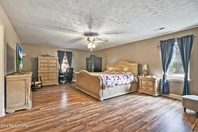 bedroom featuring a ceiling fan, visible vents, baseboards, and wood finished floors