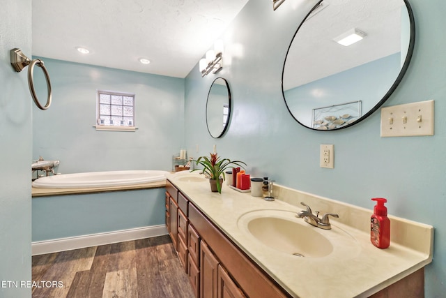 full bath featuring a garden tub, double vanity, wood finished floors, and a sink