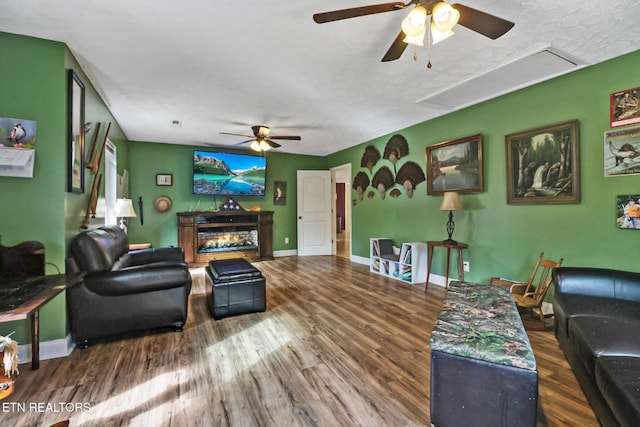 living room featuring attic access, baseboards, wood finished floors, and a lit fireplace