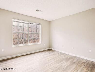 unfurnished room featuring wood finished floors, visible vents, and baseboards