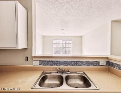 kitchen featuring a textured ceiling, light countertops, white cabinetry, and a sink