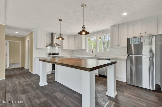 kitchen featuring backsplash, stainless steel appliances, wall chimney range hood, visible vents, and wood counters