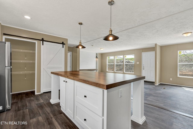 kitchen featuring dark wood-style flooring, butcher block counters, a barn door, white cabinetry, and freestanding refrigerator