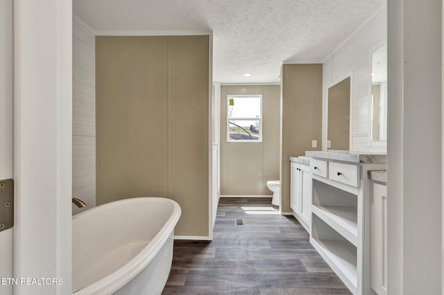 full bath featuring a freestanding tub, toilet, vanity, wood finished floors, and a textured ceiling