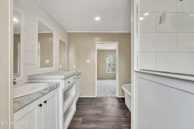 full bathroom with a textured ceiling, a soaking tub, a sink, two vanities, and wood finished floors
