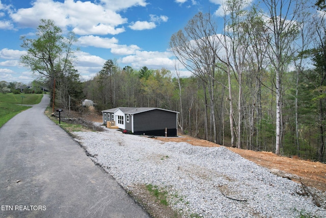 view of front of property featuring gravel driveway and a view of trees