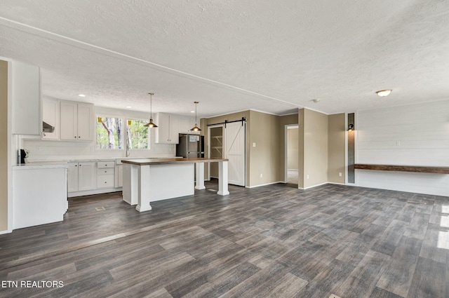 unfurnished living room featuring dark wood-type flooring, a barn door, a textured ceiling, and baseboards