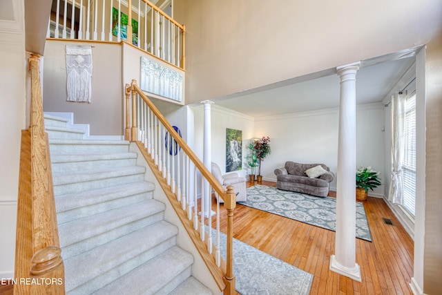 stairway featuring decorative columns, visible vents, wood-type flooring, ornamental molding, and a high ceiling