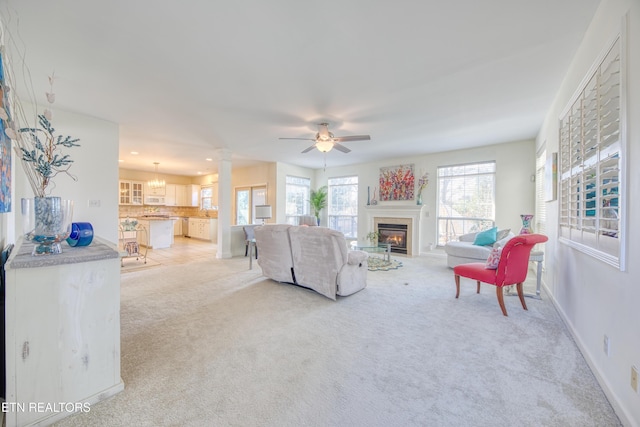 living area featuring light carpet, decorative columns, baseboards, a ceiling fan, and a glass covered fireplace