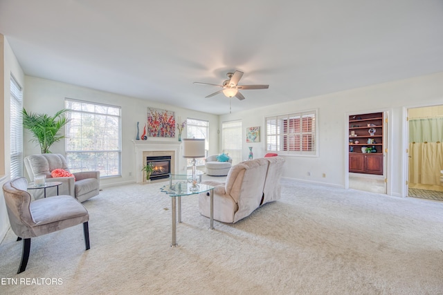 living area with a fireplace with flush hearth, carpet, ceiling fan, and baseboards