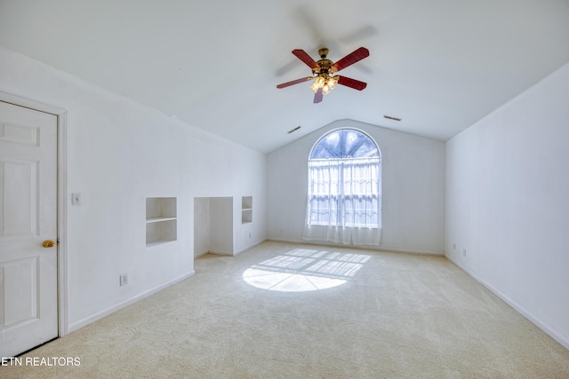 carpeted empty room featuring built in shelves, visible vents, vaulted ceiling, ceiling fan, and baseboards