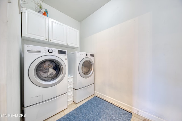 clothes washing area with light tile patterned flooring, washing machine and dryer, cabinet space, and baseboards