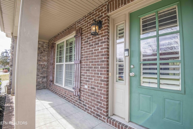 doorway to property featuring a porch and brick siding