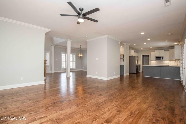 unfurnished living room with decorative columns, visible vents, dark wood finished floors, baseboards, and ceiling fan with notable chandelier