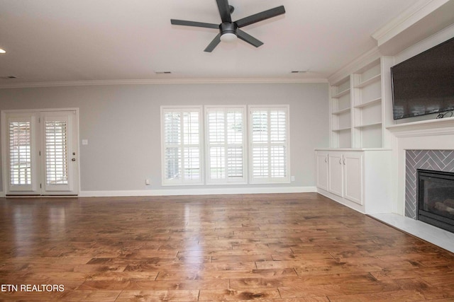 unfurnished living room featuring baseboards, a fireplace, wood finished floors, and crown molding