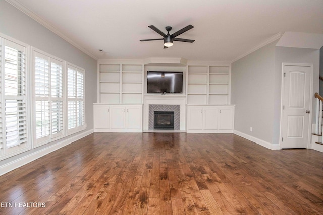 unfurnished living room featuring ceiling fan, wood-type flooring, baseboards, a tiled fireplace, and crown molding