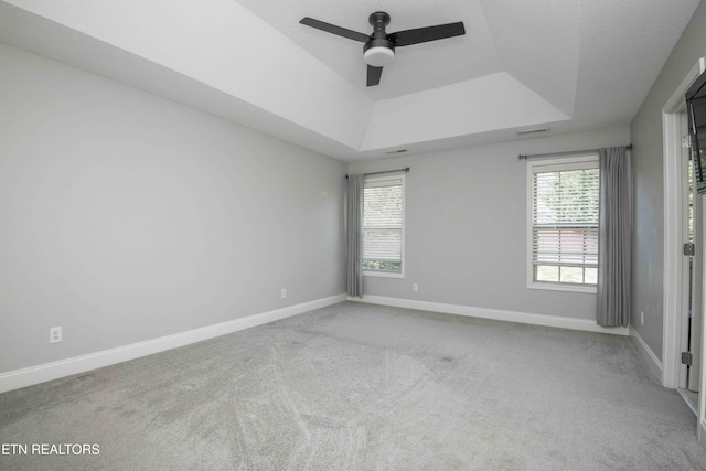 empty room featuring carpet floors, a tray ceiling, baseboards, and a ceiling fan