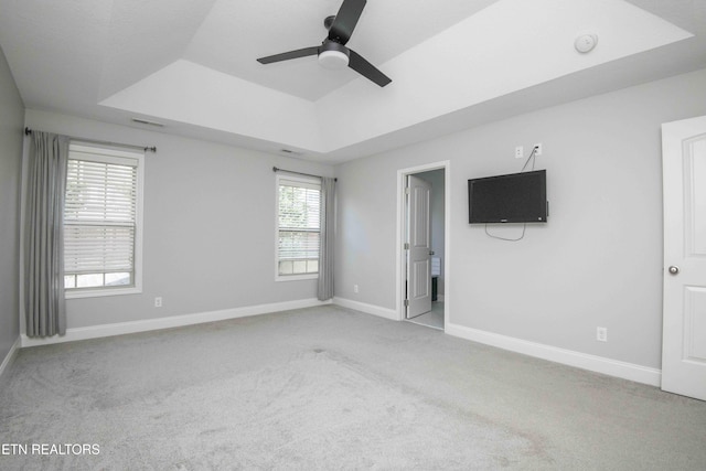 interior space featuring carpet floors, a tray ceiling, baseboards, and a ceiling fan