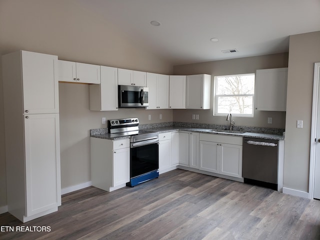 kitchen featuring a sink, visible vents, white cabinets, vaulted ceiling, and appliances with stainless steel finishes