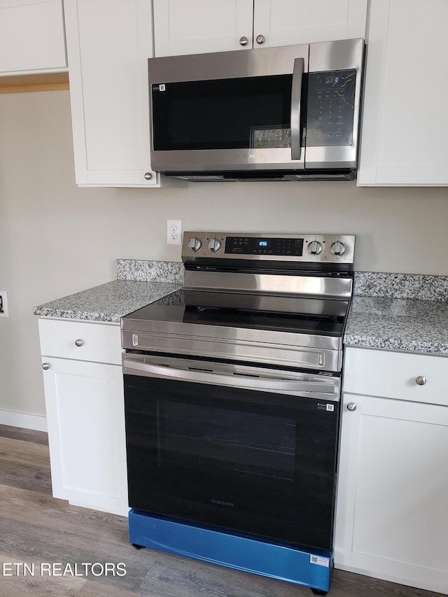 kitchen featuring light stone counters, baseboards, white cabinets, appliances with stainless steel finishes, and dark wood finished floors