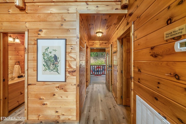 hallway with light wood-style flooring, wood ceiling, and wooden walls