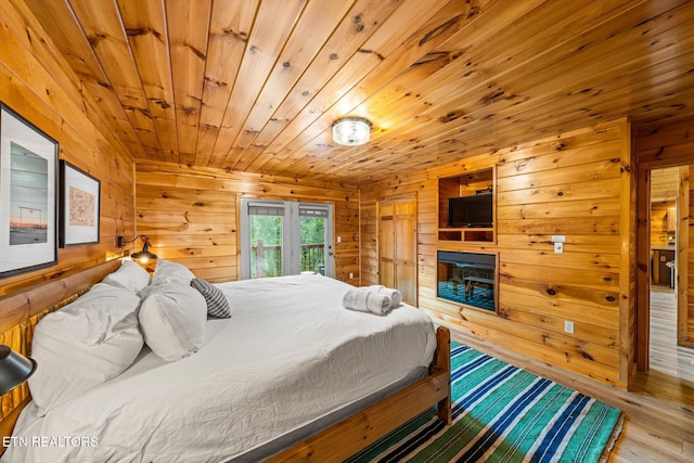 bedroom with wooden ceiling, wooden walls, access to exterior, and a glass covered fireplace