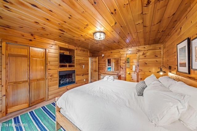 bedroom with wooden ceiling, a fireplace, wooden walls, and wood finished floors