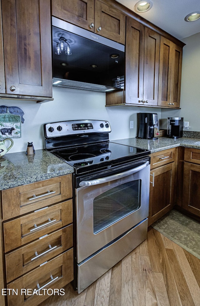 kitchen with electric range, black microwave, light wood-style flooring, and dark stone countertops